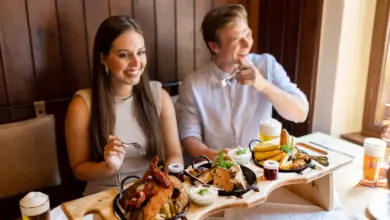 Zwei Menschen sitzen in einem Gasthaus und haben Teller mit Essen vor sich stehen. Sie wirken glücklich und lachen.
