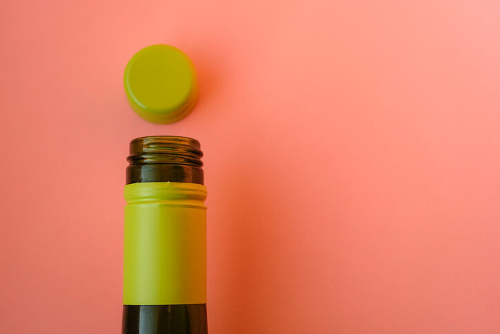 Eine grüne Weinflasche mit Schraubverschluss vor rosa Hintergrund.