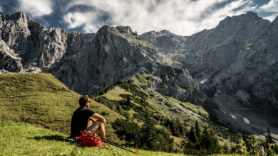 Ein Mann sitzt auf der Wiese beim Wandern und schaut auf die Berglandschaft.