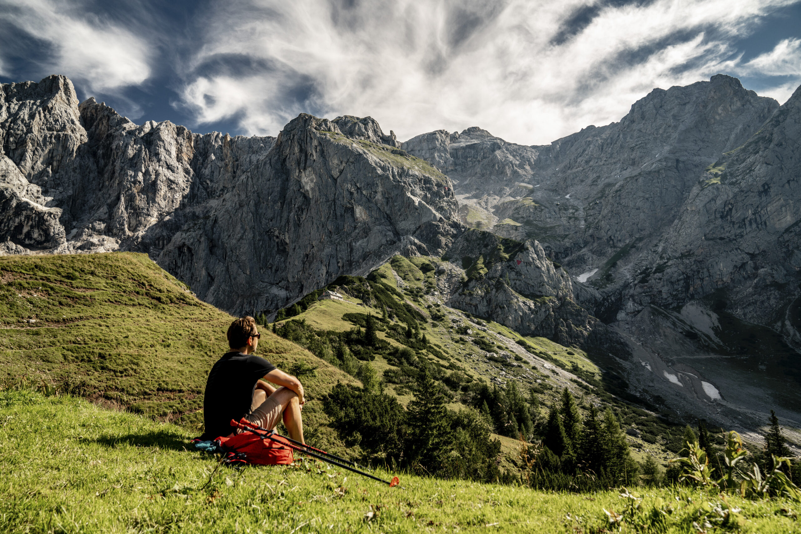 Ein Mann sitzt auf der Wiese beim Wandern und schaut auf die Berglandschaft.