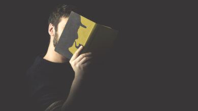 Ein Mann hält ein Buch vor sein Gesicht. Darauf zu sehen ist die Silhouette von Sherlock Holmes.