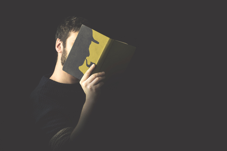 Ein Mann hält ein Buch vor sein Gesicht. Darauf zu sehen ist die Silhouette von Sherlock Holmes.