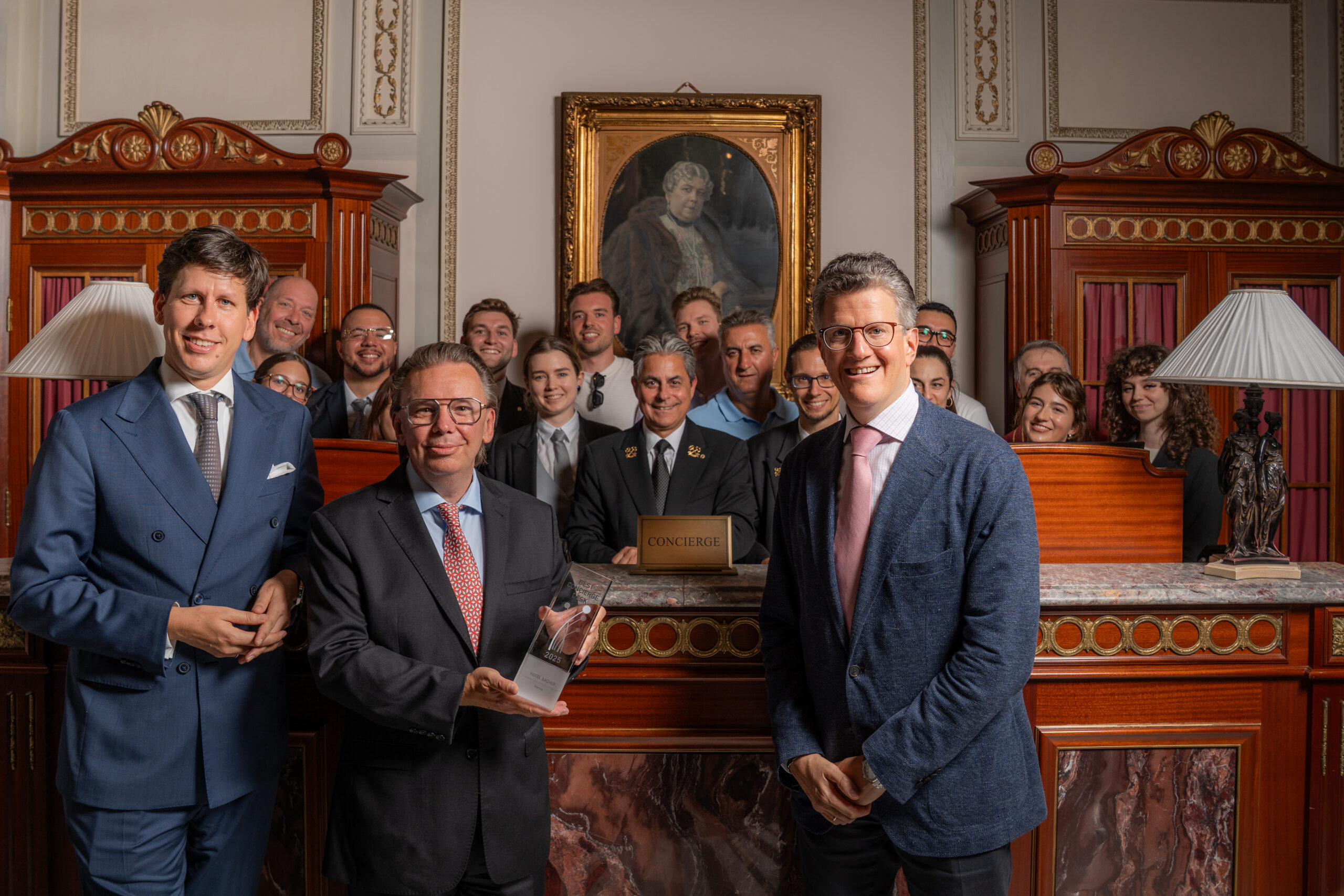 v.l.n.r. Hoteldirektor Andreas Keese, Präsident der Vereinigung Concierge Circle Luxemburg Tom Meyer und Sacher Co-Eigentümer Georg Gürtler sowie dem Concierge- und Guest-Experience-Team im Hintergrund. © Hotel Sacher